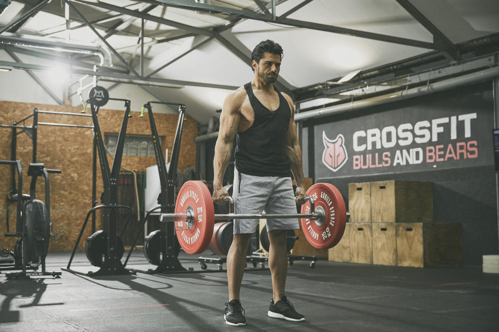 En man som tränar farmers walks med skivstång och viktskivor på ett gym