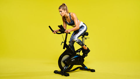 Kvinna som tränar på spinningcykel mot gul bakgrund