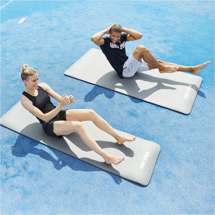 Man och kvinna som tränar utomhus på varsin träningsmatta från gorilla sprots, grå